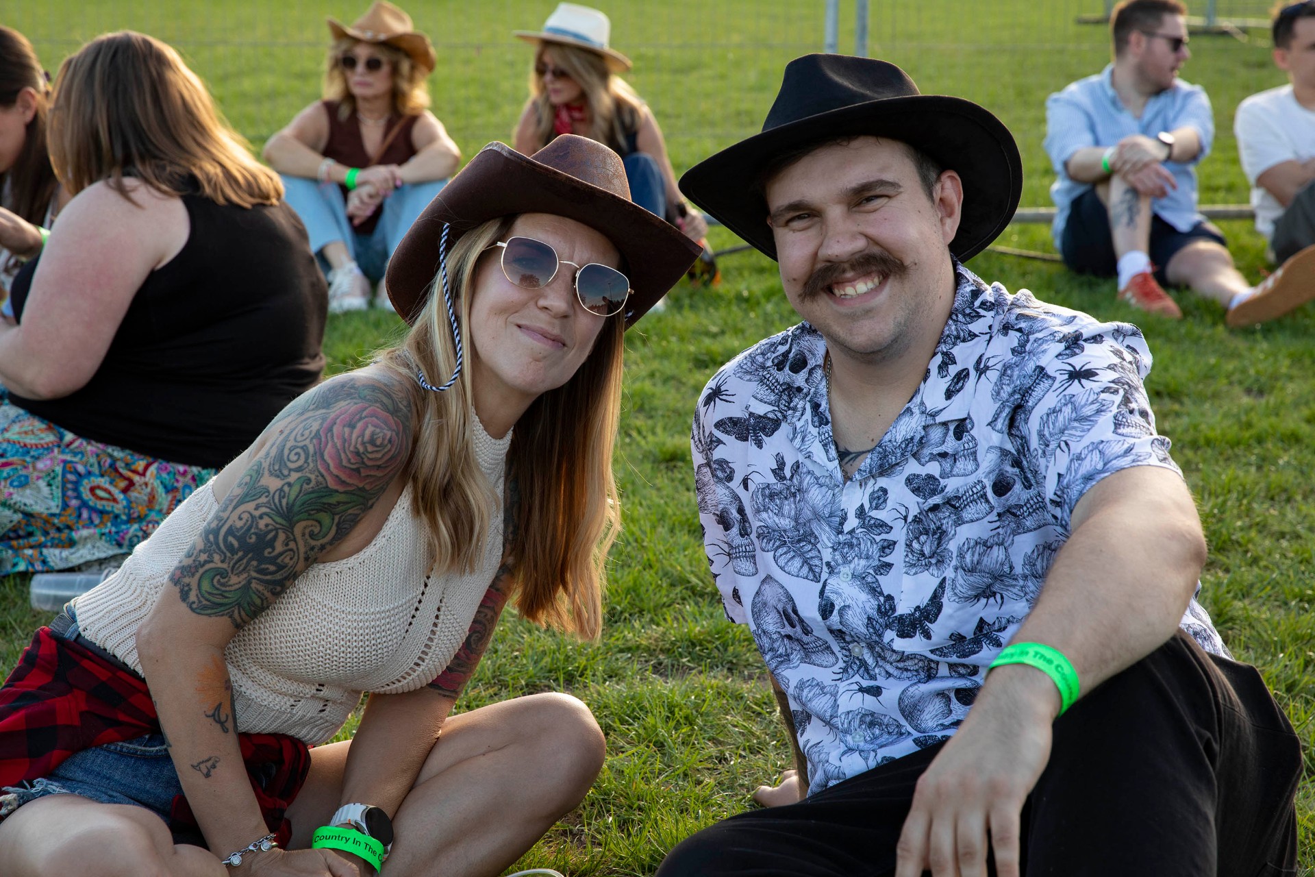Couple in cowboy hats on the grass with festival wristbands.